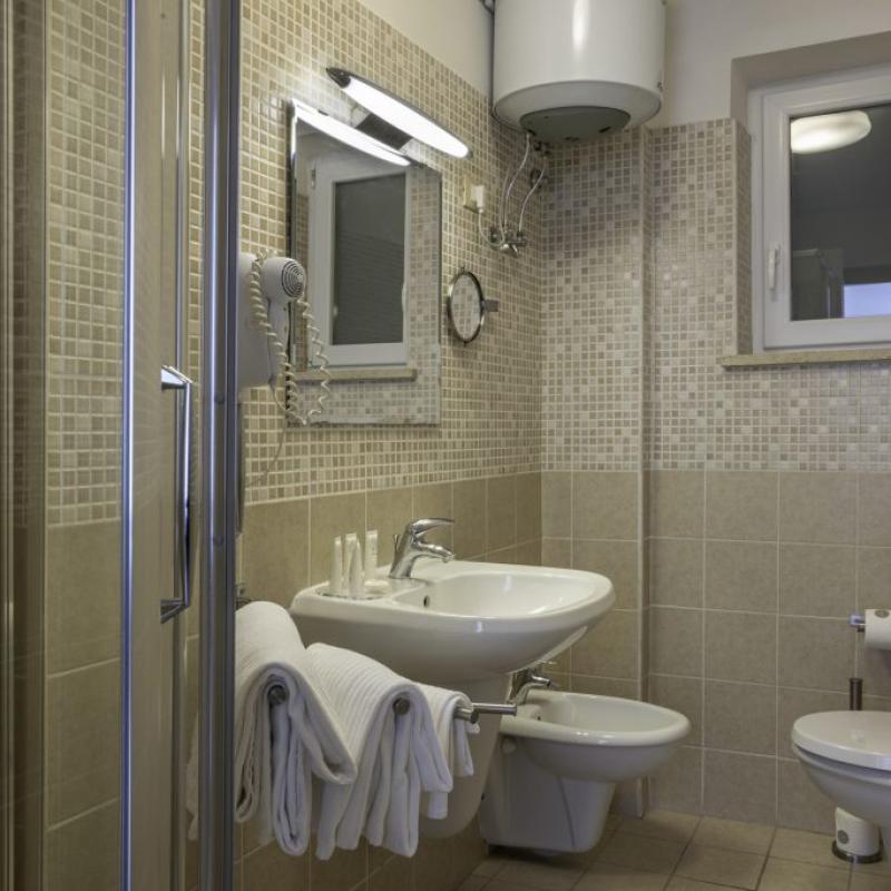 Bagno moderno con doccia, lavabo, bidet, WC, asciugamani e scaldabagno, piastrelle beige e finestra.