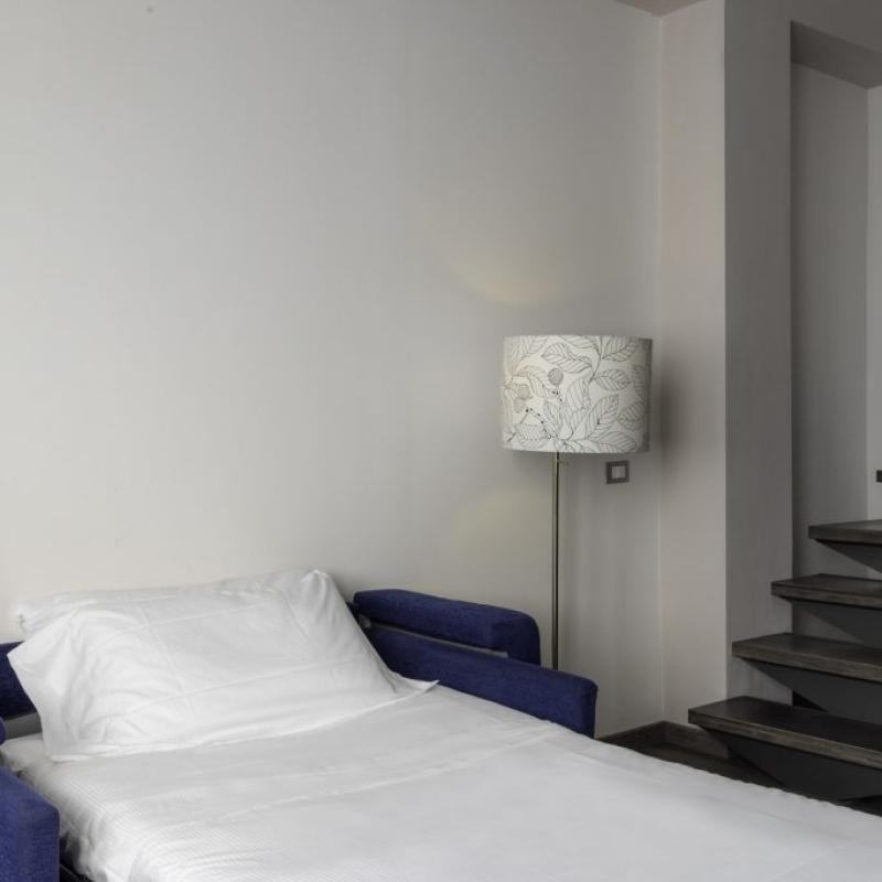Camera moderna con divano letto, lampada e scala a chiocciola.