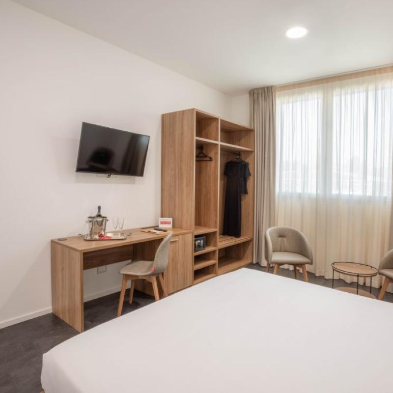 Camera moderna con letto matrimoniale, TV, scrivania e poltrone vicino alla finestra.