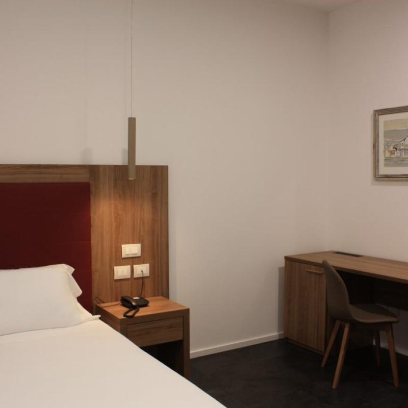 Camera moderna con letto singolo, scrivania in legno e quadro appeso alla parete.