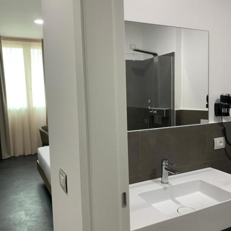 Bagno moderno con lavandino bianco, specchio grande e vista su camera da letto.