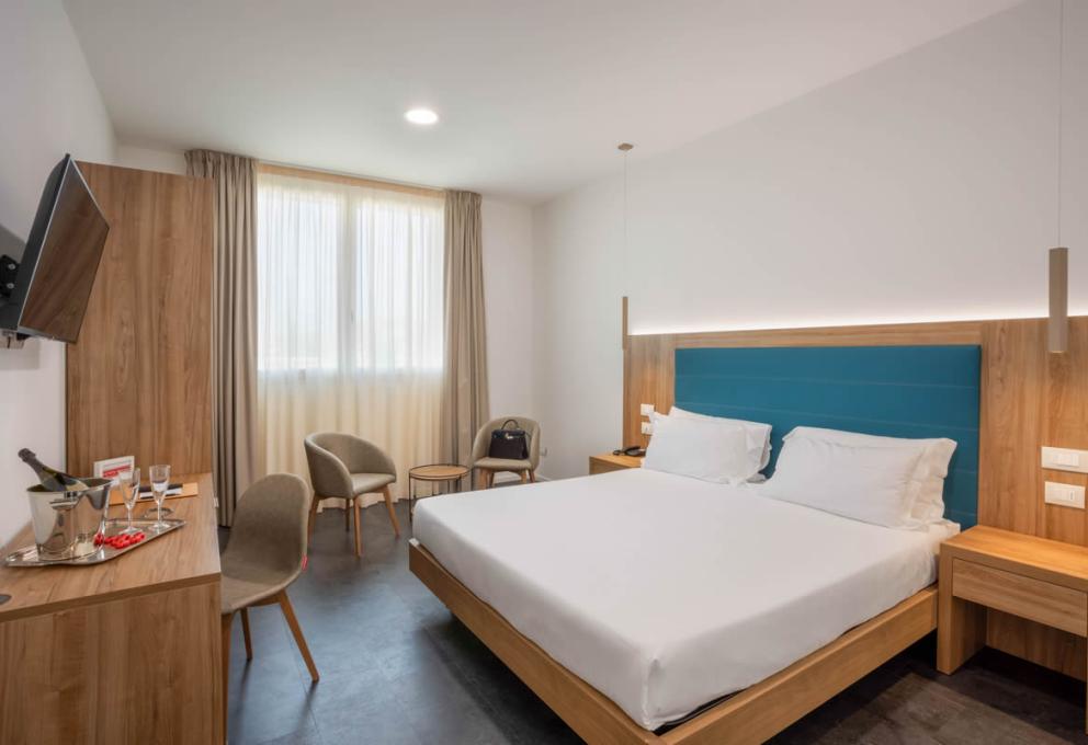 Camera moderna con letto matrimoniale, TV, tavolo, sedie e finestra con tende.