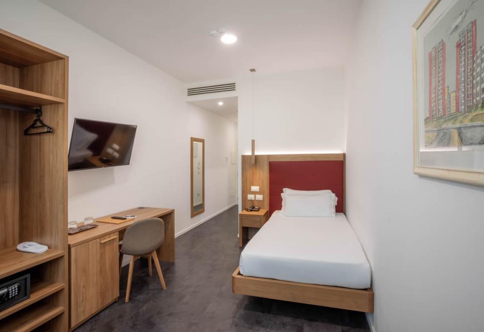 Camera moderna con letto singolo, scrivania, TV a schermo piatto e arredi in legno.