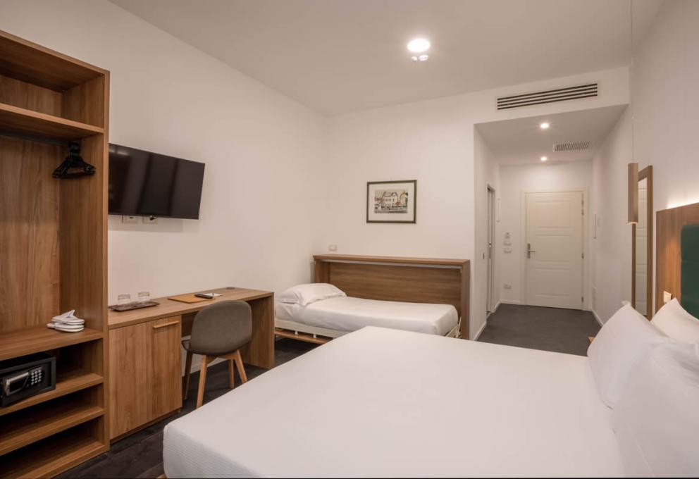 Camera moderna con letto matrimoniale, letto singolo, scrivania, TV e armadio aperto.