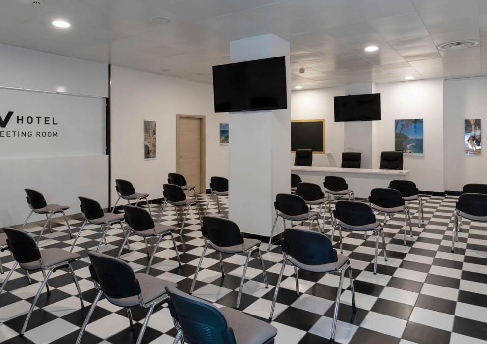 Sala riunioni dell'hotel con sedie nere e pavimento a scacchi bianchi e neri.